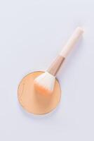 A sample of a round block of compact powder in a natural tone and a chic brush for applying makeup. vertical top view. layout for design. photo