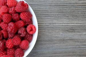 red raspberries in a bowl on the left, gray wooden table background copy space on the right. photo
