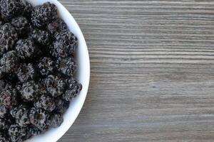 black raspberries in a bowl on the left, gray wooden table background copy space on the right. photo