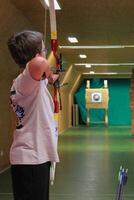 Boy with a bow and an arrow aiming at a target at an inside archery shooting range. photo