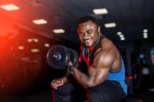 Smiling afro american sports man looking at camera over black background with dumbbell in hand. Perfect muscular body with strong muscles. photo