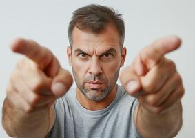 Serious Man Pointing Fingers Forward, Intense Expression, Close-Up Portrait, Isolated Background, Horizontal View, Strong Eye Contact, Determined Pose, Mid-30s Male, Casual Grey T-Shirt photo