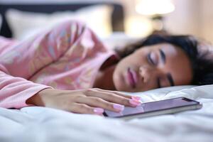 Woman Sleeping on Bed with Phone in Hand, Cozy Ambience, Soft Light, Peaceful Moment, Relaxation, Unplugged Life, Intimate Setting, Night Routine, Serenity at Home photo