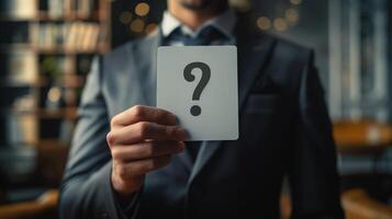 Businessman Holding Question Mark Card in Hand - Mystery, Uncertainty, and Decision Making Concept in Office Environment, Blurred Background with Bookshelves and Lights photo