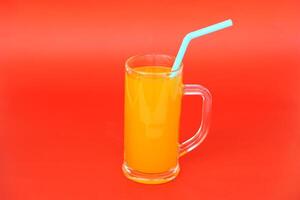 Glass mug of orange juice with drinking straw. Red background. Concept, morning refreshing beverage. Sweet, testy and high vitamin C. photo