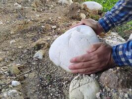 Close up man hands tries to pull up the big stone from ground. Concept, heavy. Hard working. Strong body to lift or move heavy rock. photo