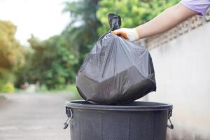 Hand holding garbage black bag putting in to the bin. Concept, garbage management, Keep clean for sanitary and community service for the best environment. Zero waste. photo