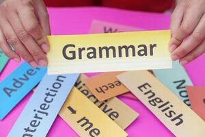 Close up student hands hold paper word card with text Grammar. Concept, English language grammar teaching. Using word card to create for playing educational fun games or practice photo