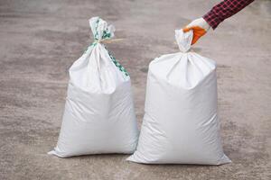 Close up man holds white polypropylene sack that contain full of agricultural grains, tied on the top with bamboo rope. Concept, reusable bag for contain crops, fertilizer or others. photo