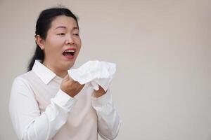Asian woman is sneezing, open mouth, holds white tissue paper. Concept, Health problems. Ill, sick and flu. Cover mouth when cough or sneeze to stop spreading of germs, disease photo