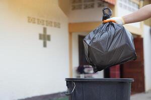 Hand holding garbage black bag putting in to the bin. Concept, garbage management, Keep clean for sanitary and community service for the best environment. Zero waste. photo