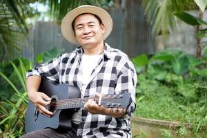 Handsome Asian man listen to music and playing the guitar in garden with cozy atmosphere. Concept, Relax time with music. Happy lifestyle. Love music. Hobby and pastime photo