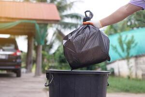 Hand holding garbage black bag putting in to the bin. Concept, garbage management, Keep clean for sanitary and community service for the best environment. Zero waste. photo