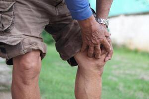 Close up elderly man hurt his knee, use hands to massage knee. Concept, health care and health problems. Artritis symptom. Suffering from knee pain. Tendon problems and Joint inflammation photo
