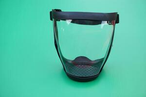 Protective safety face shield, Clear glass with black edge. Green background. Concept, tool, equipment use for wearing with face to protect from dust, germ spreading or others into face. Work Secured. photo