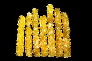 A row of yellow sticks with a black background. The sticks are made of sugar and are arranged in a line photo