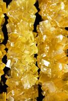 The sticks are made of sugar and are arranged in a line. A row of yellow crystals are lined up on a black surface. The crystals are all different sizes and shapes photo