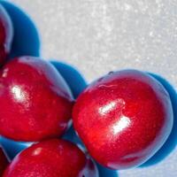 A bunch of red cherries are arranged in a circle on a blue background. The cherries are shiny and ripe, and they seem to be the main focus of the image photo