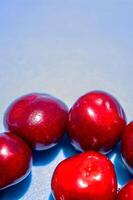 A bunch of red cherries are arranged in a circle on a blue background. The cherries are shiny and ripe, and they seem to be the main focus of the image photo
