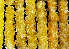 The sticks are made of sugar and are arranged in a line. A row of yellow crystals are lined up on a black surface. The crystals are all different sizes and shapes photo