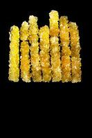A row of yellow sticks with a black background. The sticks are made of sugar and are arranged in a line photo