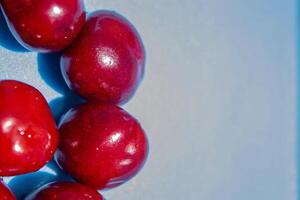A bunch of red cherries are arranged in a circle on a blue background. The cherries are shiny and ripe, and they seem to be the main focus of the image photo