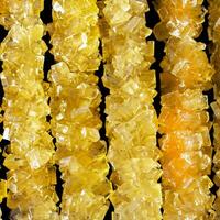 The sticks are made of sugar and are arranged in a line. A row of yellow crystals are lined up on a black surface. The crystals are all different sizes and shapes photo