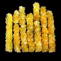A row of yellow sticks with a black background. The sticks are made of sugar and are arranged in a line photo