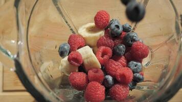 Adding raspberries, blueberries and bananas to a blender to make a smoothie. The smoothie ingredients are ready to be blended. video