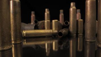 A group of spent brass cartridge casings are scattered on a black mirror surface.. The casings are arranged in various positions, some standing upright, others lying on their sides video