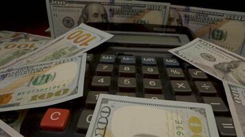 A calculator sits on a pile of US dollar bills. The calculator's display shows a number, and the buttons are visible. video