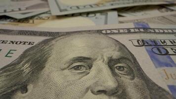 A close-up shot of a US one hundred dollar bill, focusing on the portrait of Benjamin Franklin. The bill is lying flat on a surface, and the camera slowly pans across Franklin's face. video