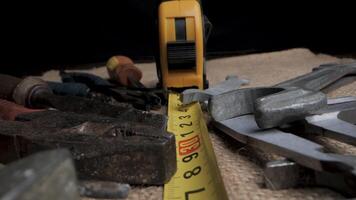A variety of tools, including a hammer, wrenches, pliers, and a tape measure, are spread out on a fabric surface. The tape measure is centered in the frame and extends past several of the tools. video