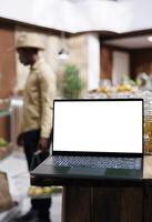 Close-up shot of a laptop with an isolated white screen display placed on a counter. Detailed view of a blank chromakey mockup template found on a wireless computer at a modern grocery store. photo