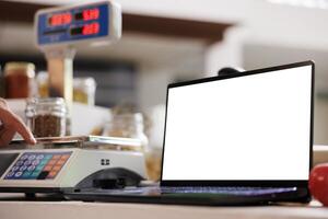 Close-up of laptop at cashier desk, showing isolated chromakey copyspace template. In local eco friendly market, digital laptop displaying blank white screen for advertising. photo