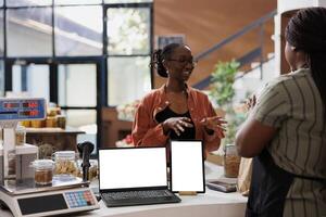 Woman purchases organic items at checkout, while digital device remains blank with a white screen. Simultaneously, laptop and tablet displays mockup template, awaiting content for bio store promotion. photo