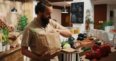 Dolly in close up shot of man in zero waste supermarket using nonpolluting paper bag while shopping for vegetables. Client in local shop using no single use plastics policy for CO2 emissions reduction photo