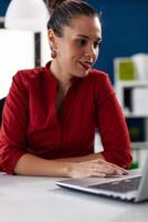 View of businesswoman typing on laptop and using touchped, in corprate business workplace building. Manager looking through documents in start up company. Director checking notest on notebook. photo