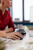 Closeup of hand using wireless computer mouse in startup office. Entrepreneur fingers with ring cliking at desk. Manager in red shirt scrolling content on desktop computer in company worskpace. photo