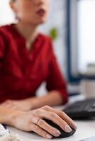 Closeup of employee hand in red shirt using wireless computer mouse. Manager fingers with ring cliking at desk in startup office. Entrepreneur scrolling content on desktop computer. photo