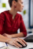 Closeup of manager fingers with ring cliking at desk in startup office. Employee scrolling content on desktop computer. Entrepreneur hand in red shirt using wireless computer mouse. photo