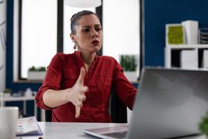 Businesswoman in red shirt looking indignant at laptop. Entrepreneur having unexpected notebook computer problems. Startup owner sitting at desk disappointed by business results. photo