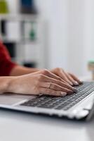 Closeup of startup manager hands typing on laptop. Detail of employee fingers resting on notebook computer keyboard in start up office. Businesswoman in red shirt shopping online at work desk. photo