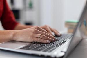 Closeup of small business owner hands typing on laptop. Detail of businesswoman fingers resting on notebook computer keyboard in startup office. Manager in red shirt browsing internet at work desk. photo