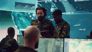 Diverse team of infantry unit leader and commander gather intelligence via radar surveillance, examine a world map to ensure national safety. Officers operating in mission control center. Camera A. video