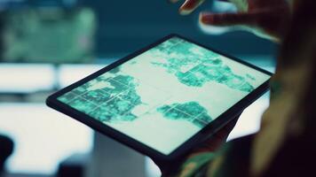 Army soldier reviews targets on a satellite world map to ensure global protection, works on tablet in military command center. Private examines battlefield data for intelligence. Close up. Camera A. video