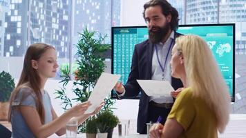 Financial advisor showing statistical graphs on big screen to customers, analyzing market trends to optimize income. Family members checking investment plan on display made by consultant, camera B video