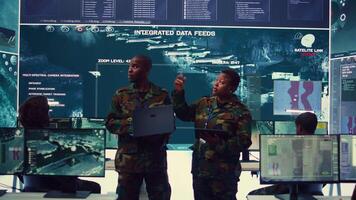 Sergeant major and female soldier checking real time field data in command post monitoring room, examining missions and operations. Team of troops interprets satellite imagery. Camera B. video