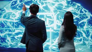 Engineer wearing VR headset looking at hologram of artificial intelligence human brain simulation, assisted by colleague. IT specialist and coworker interacting with AI visualization, camera B video