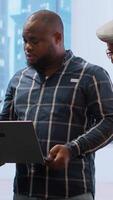 Vertical Real estate broker presenting a new high class office space to clients, discussing blueprints using a tablet during the office tour. Planning investment strategy involving property. Camera B. video